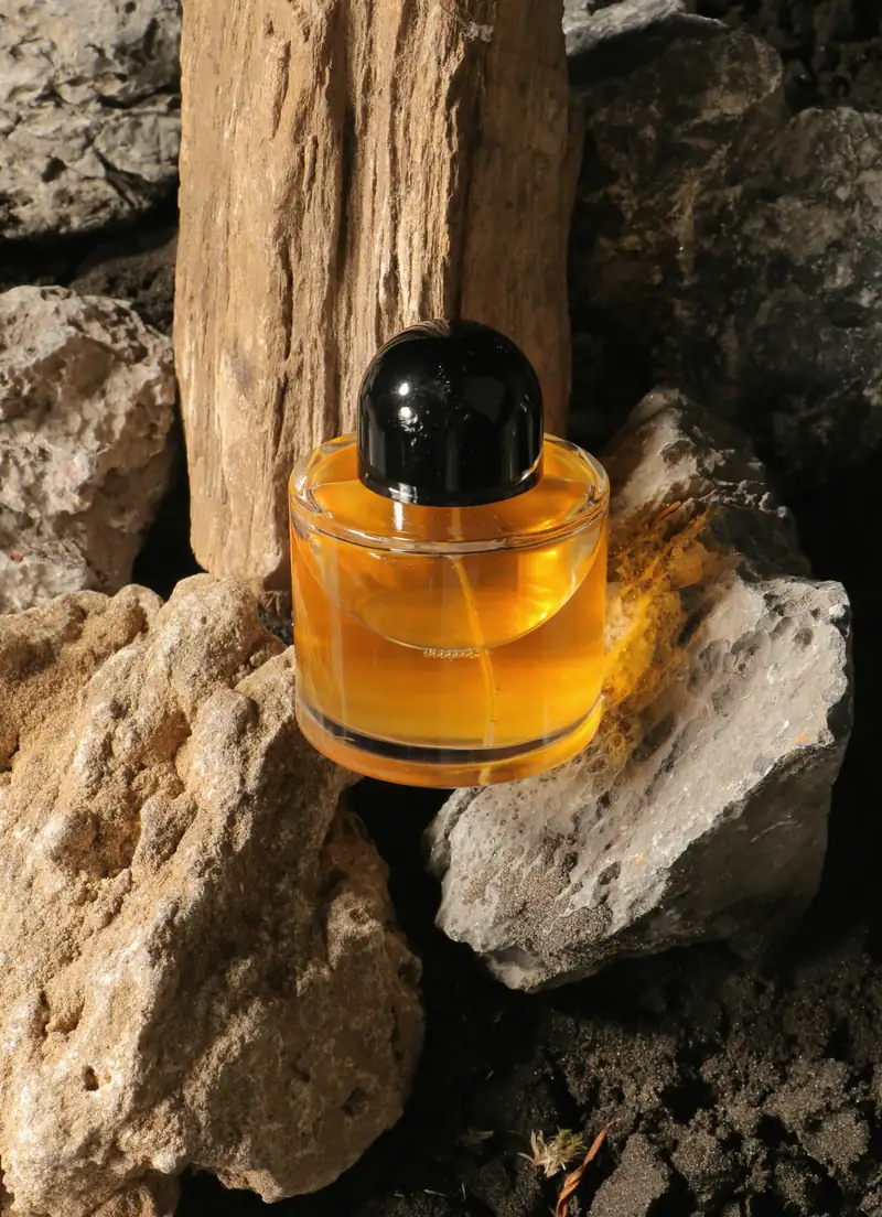 Frasco de perfume ámbar con tapa negra entre rocas
