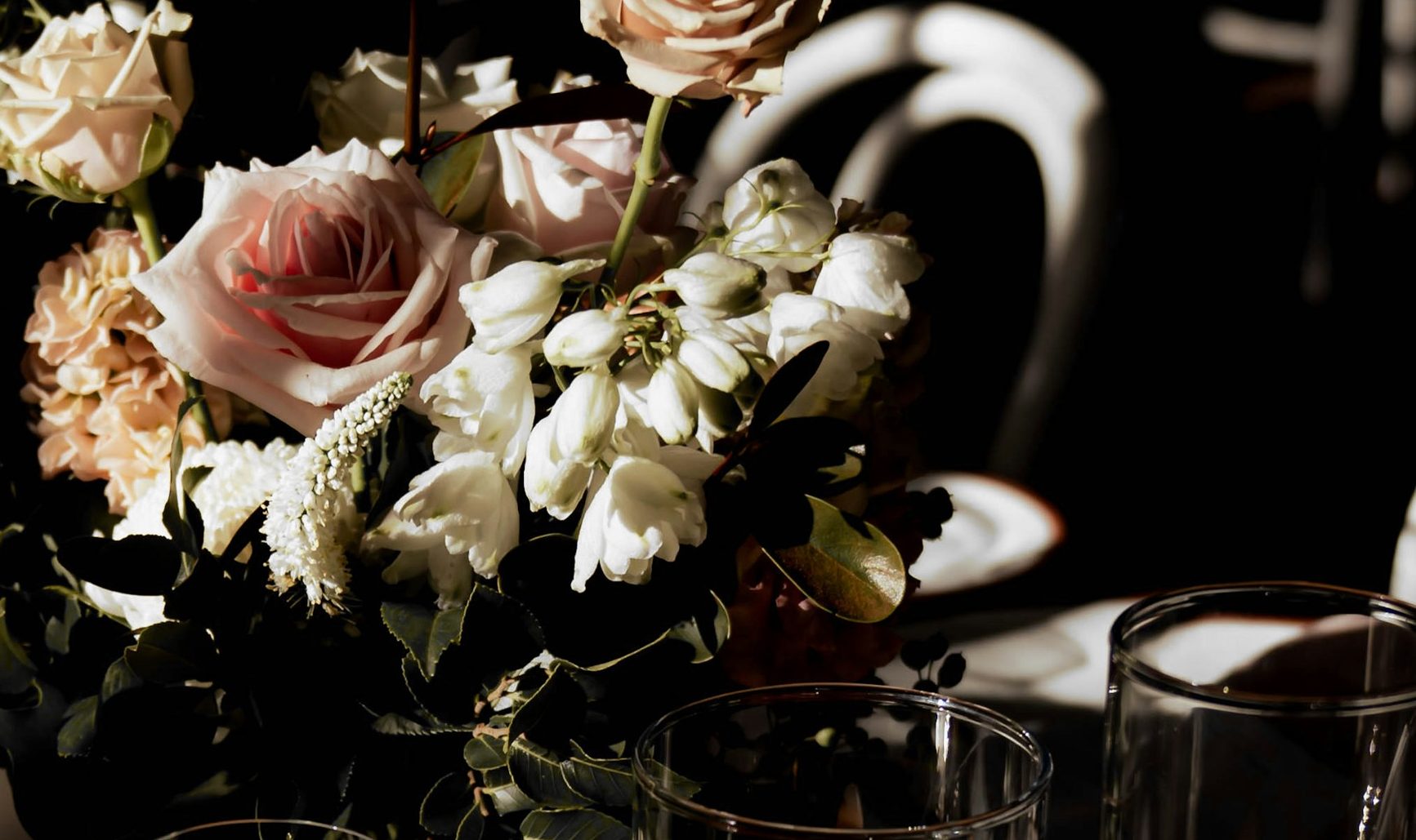 Mesa a media luz con rosas, copas y una vela