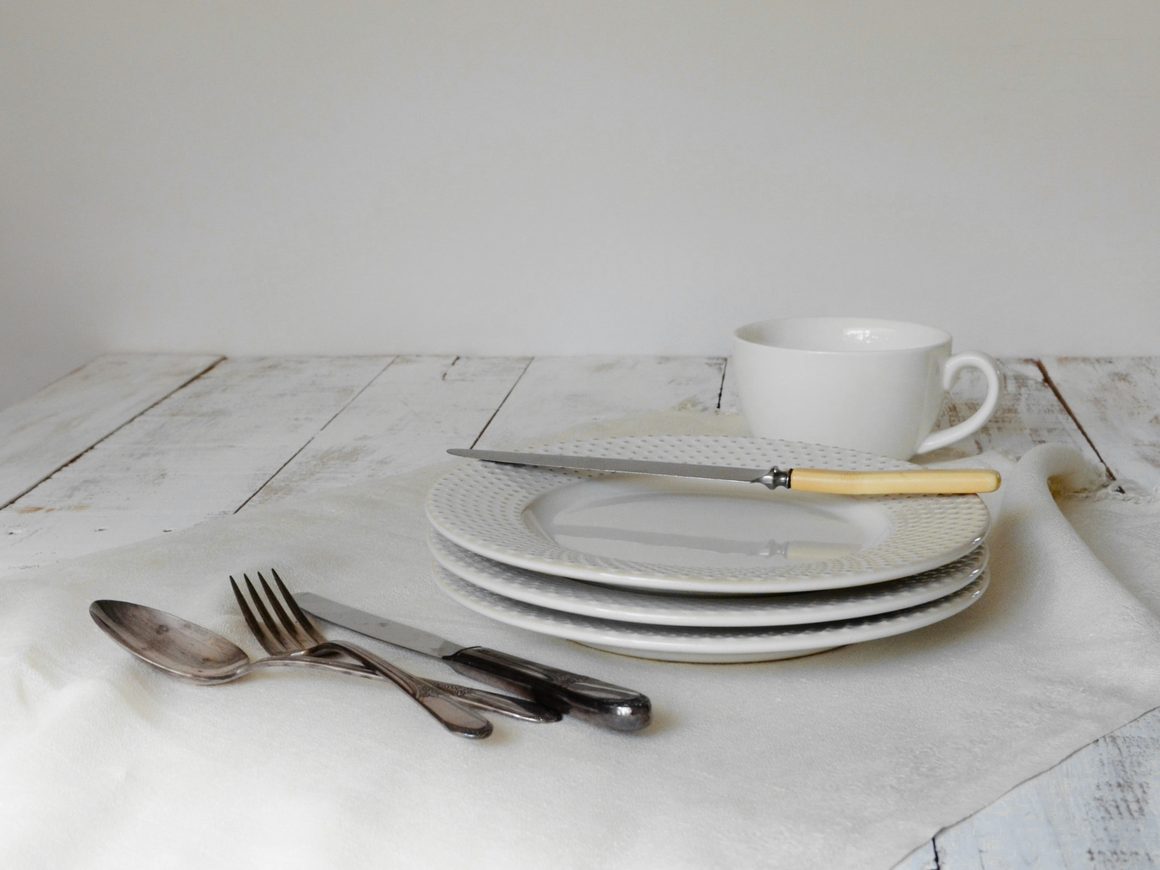 Cuchara, tenedores y platos blancos sobre un mantel de lino
