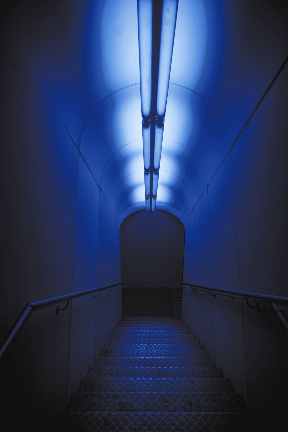 Un pasillo largo con tubos de luz en el techo, en tonos de azul