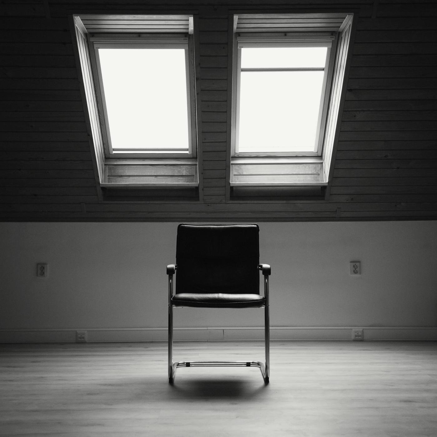 Una silla vacía en el centro de un desván, bajo dos claraboyas, en blanco y negro