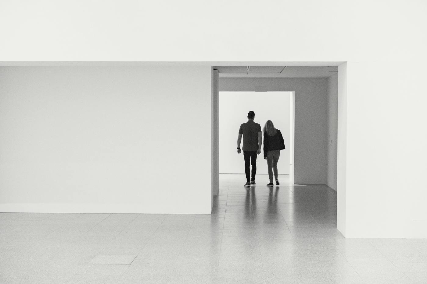 Dos visitantes, de espaldas, cruzan el vano de una sala blanca