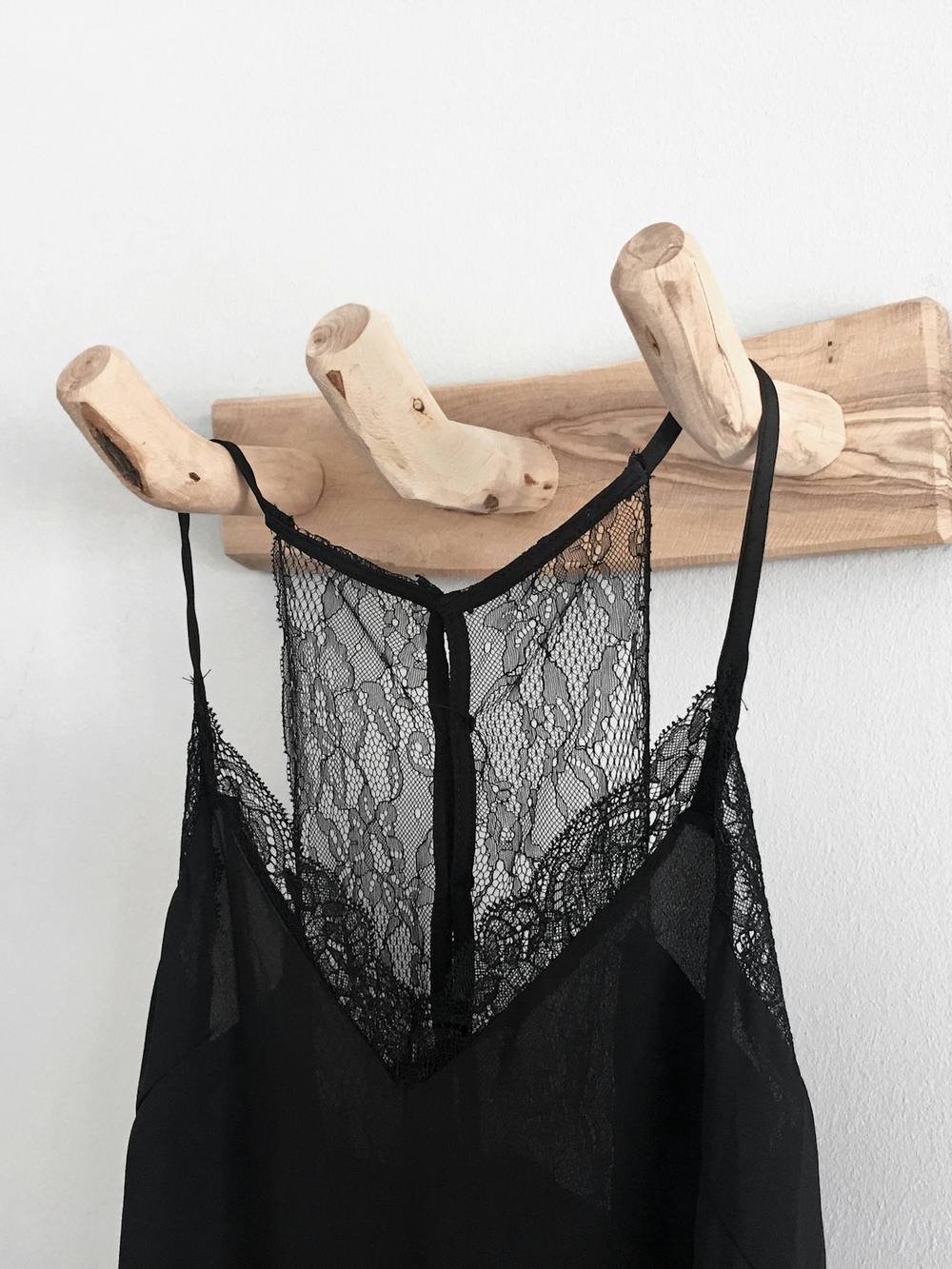 Camisola negra de encaje colgada de una percha de madera sobre un muro blanco