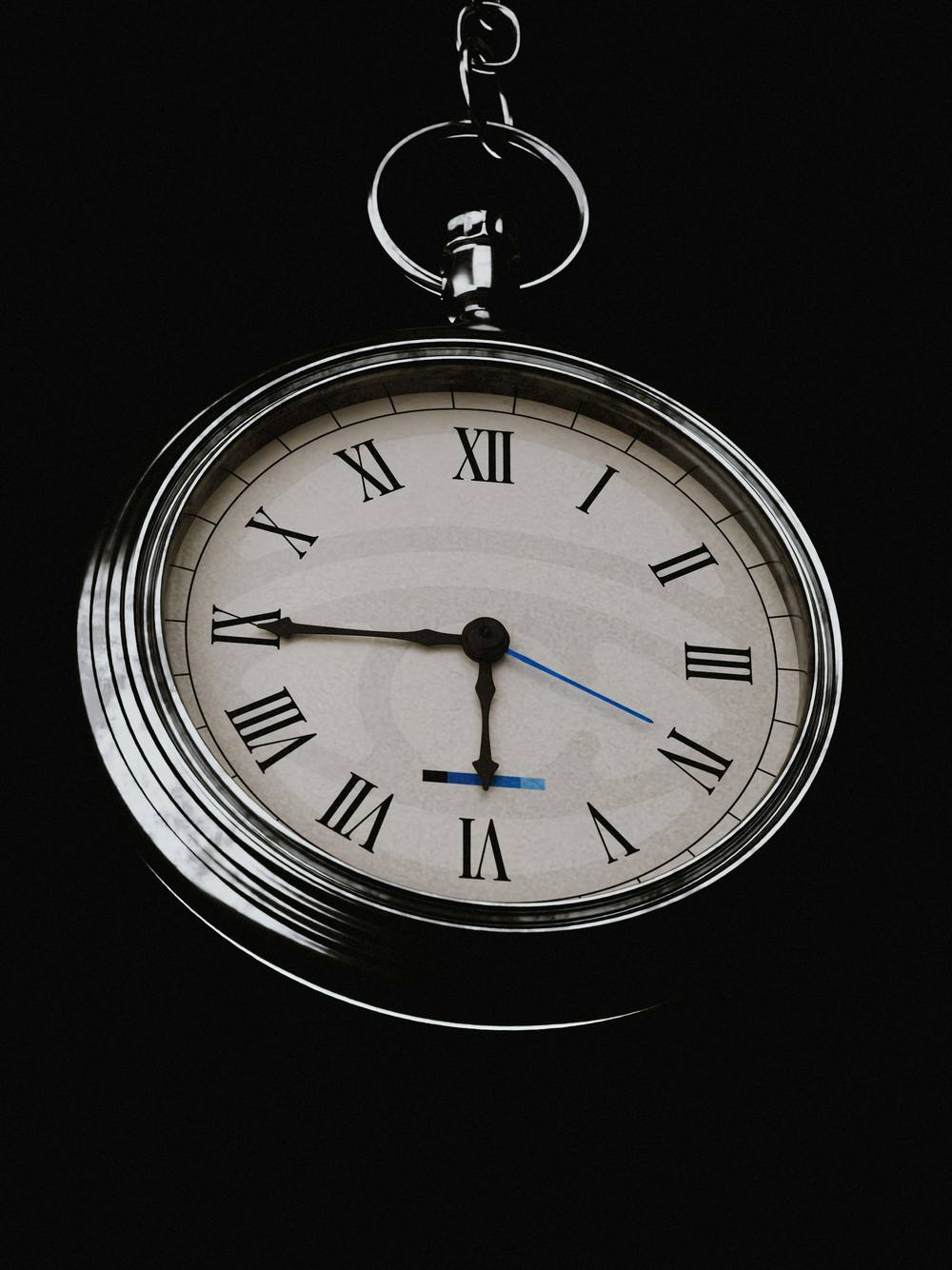 Reloj de bolsillo con números romanos colgando de su cadena sobre fondo negro