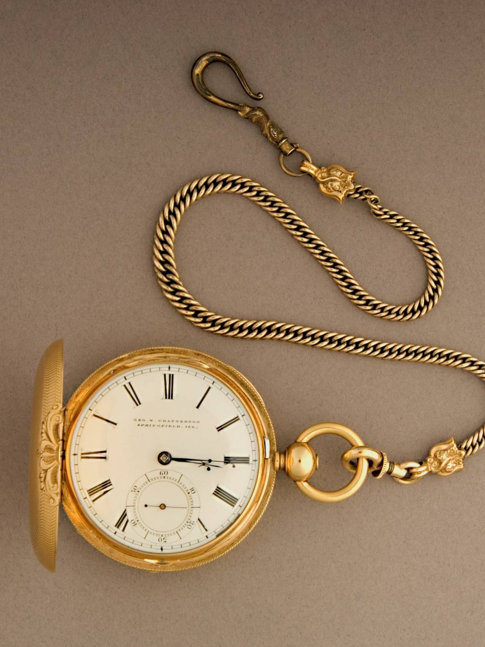 Reloj de bolsillo dorado con su cadena sobre un fondo beige