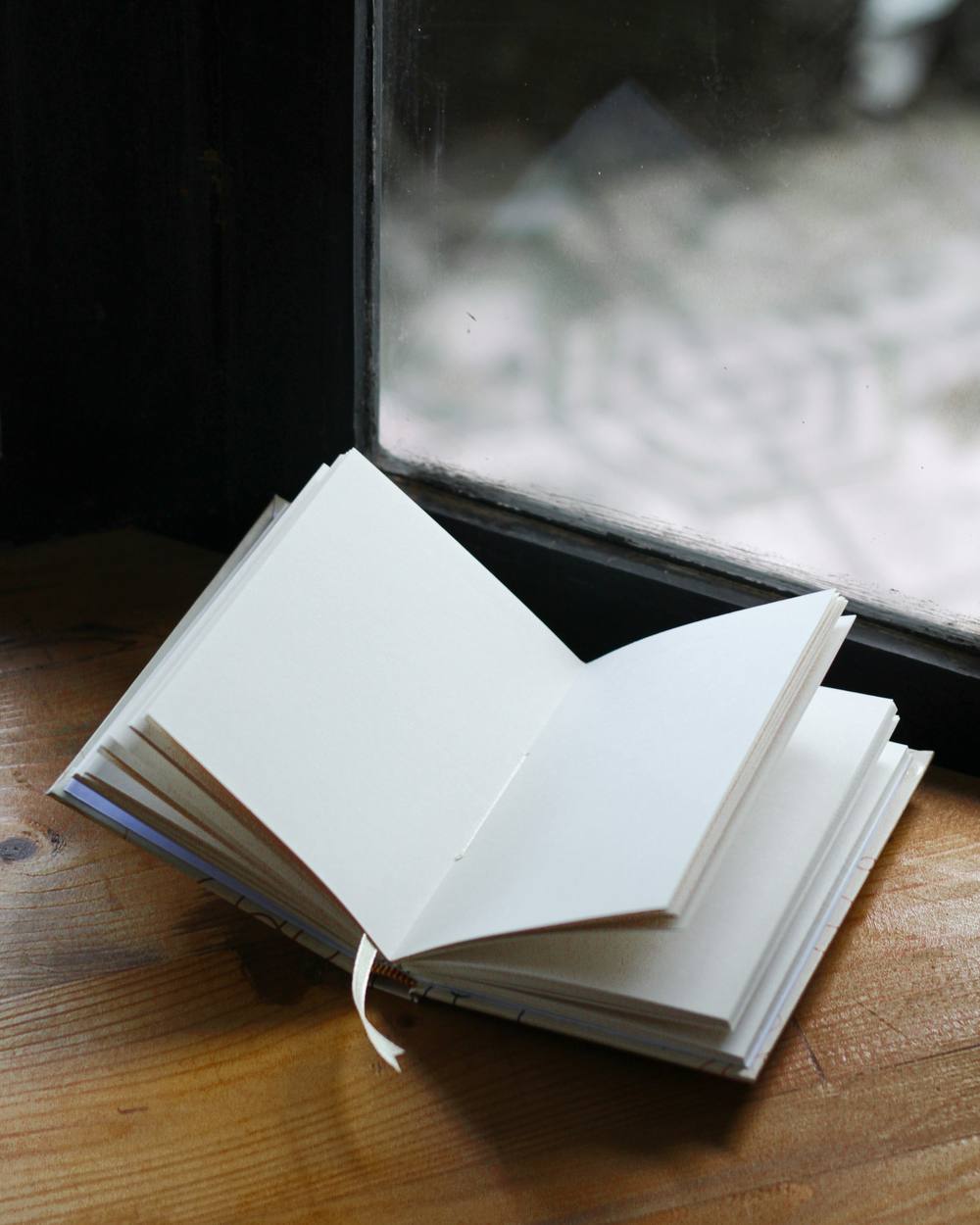 Cuaderno pequeño abierto sobre madera, junto a una ventana