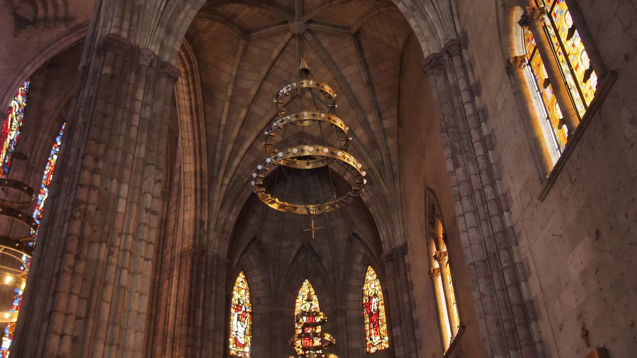 Bóvedas de piedra de una iglesia con vitrales de colores y una lámpara colgada en el centro