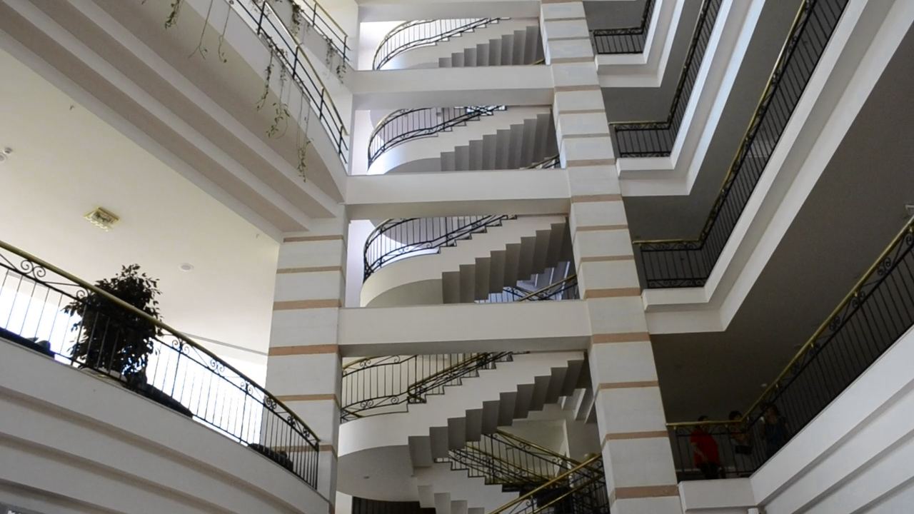 Vista hacia arriba de una escalera blanca con barandas y pasamanos de latón que gira alrededor de un patio de luz
