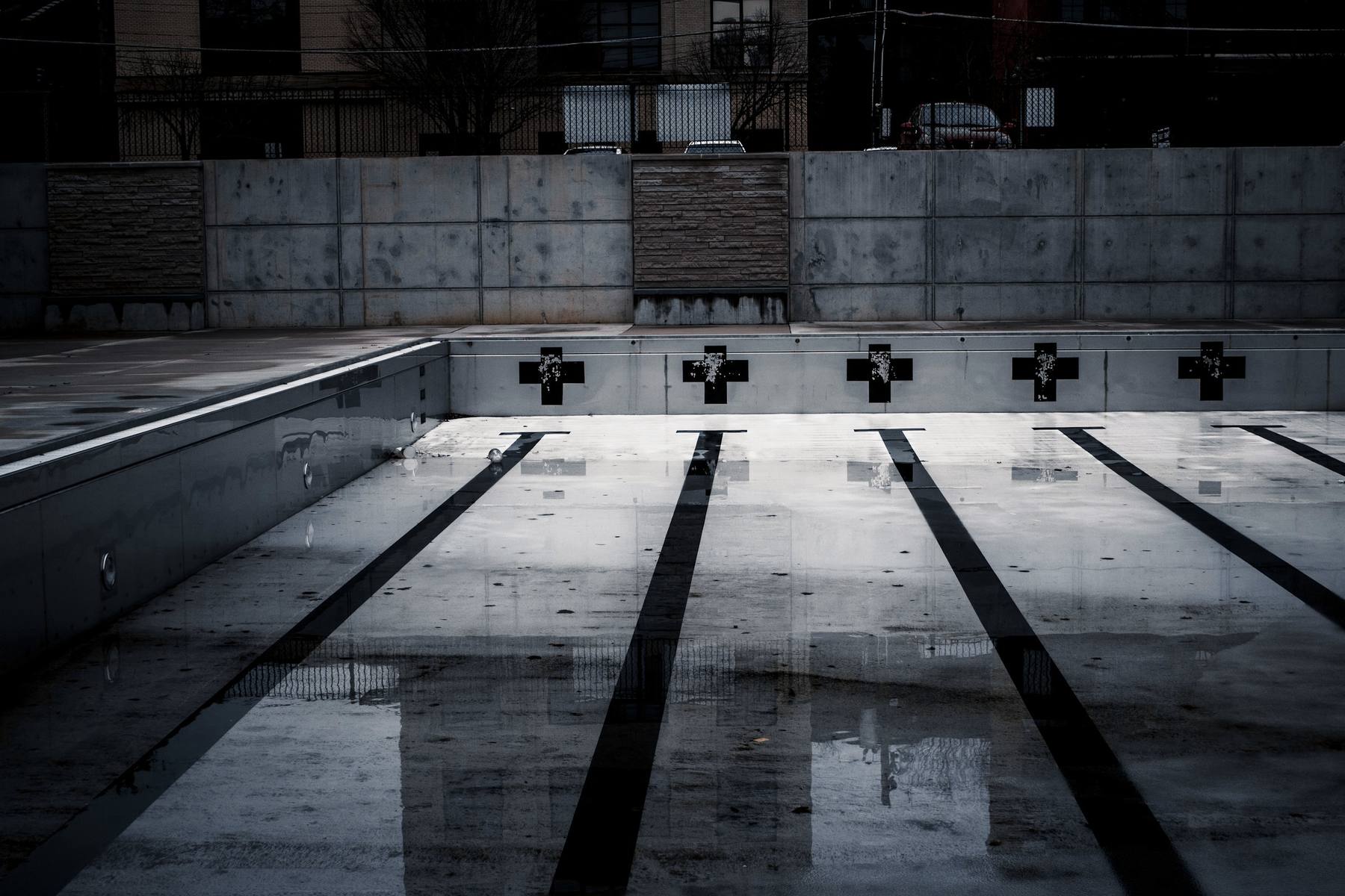 Piscina cubierta de hormigón con calles oscuras marcadas en el fondo y reflejos sobre el agua quieta