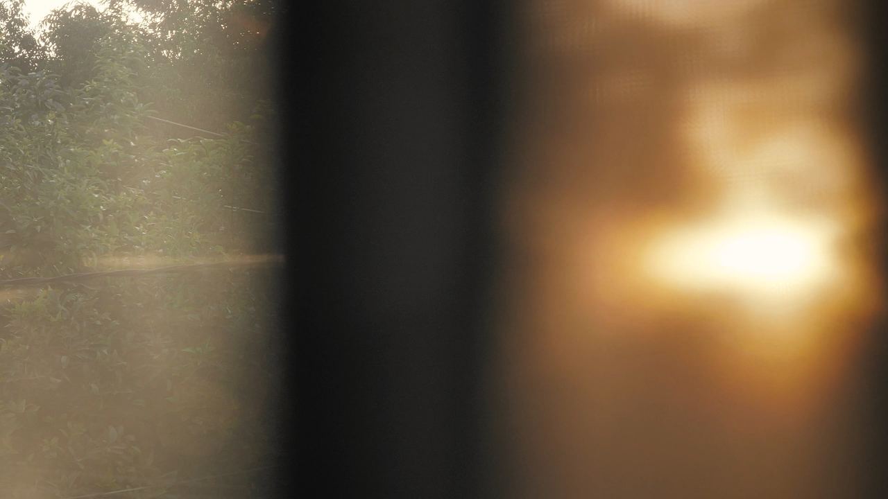 Ventana con una cortina clara y una luz cálida que se difumina sobre el paisaje del fondo