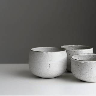 Tres cuencos blancos de gres moteado sobre una mesa blanca