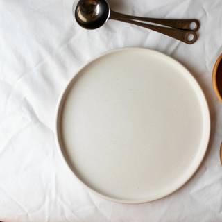 Plato crema y dos cuencos pardos sobre un mantel blanco, vistos desde arriba