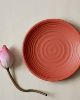 Plato de barro rojizo con relieve de círculos, junto a una flor rosada