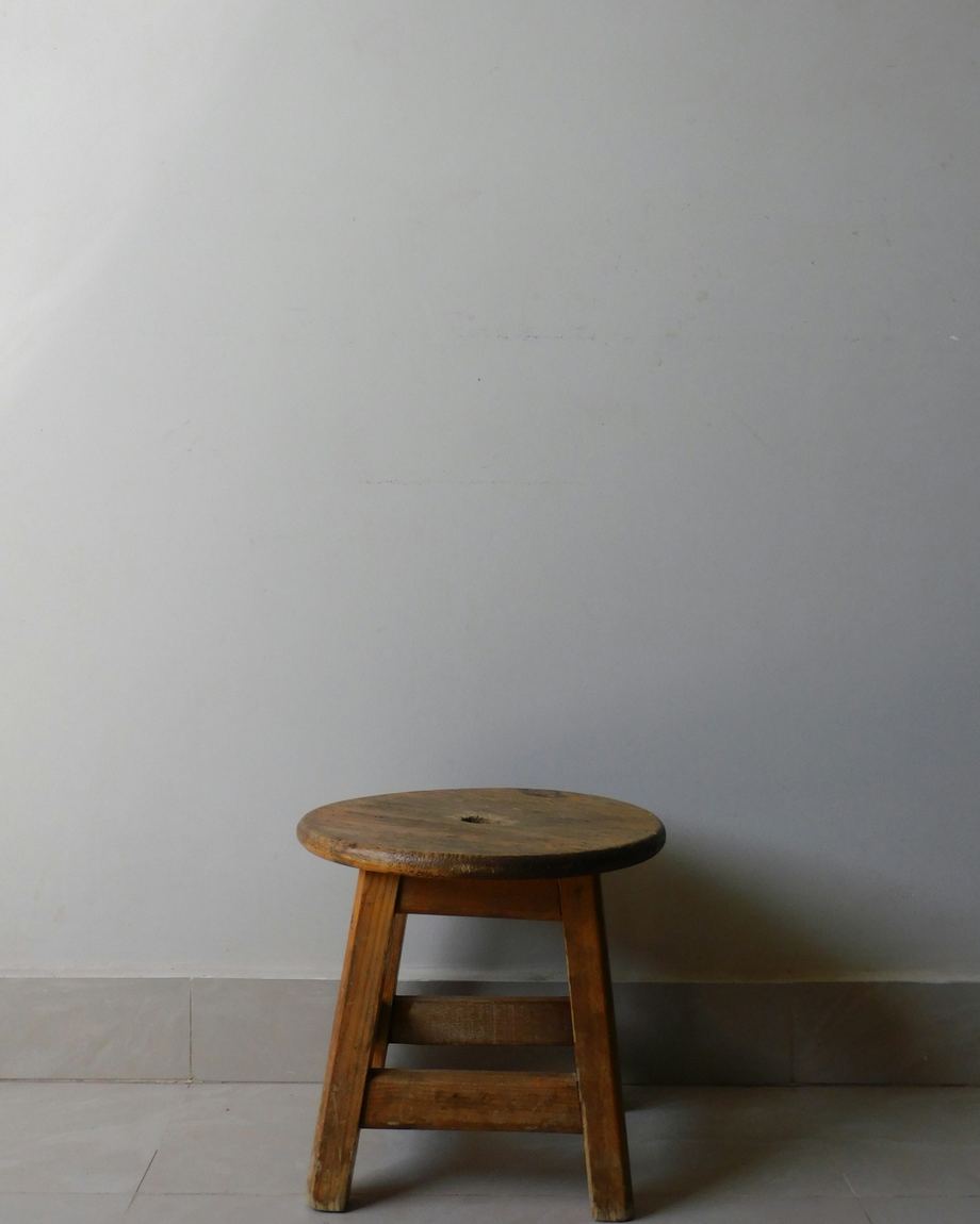Banco bajo y redondo de madera antigua junto a una pared gris