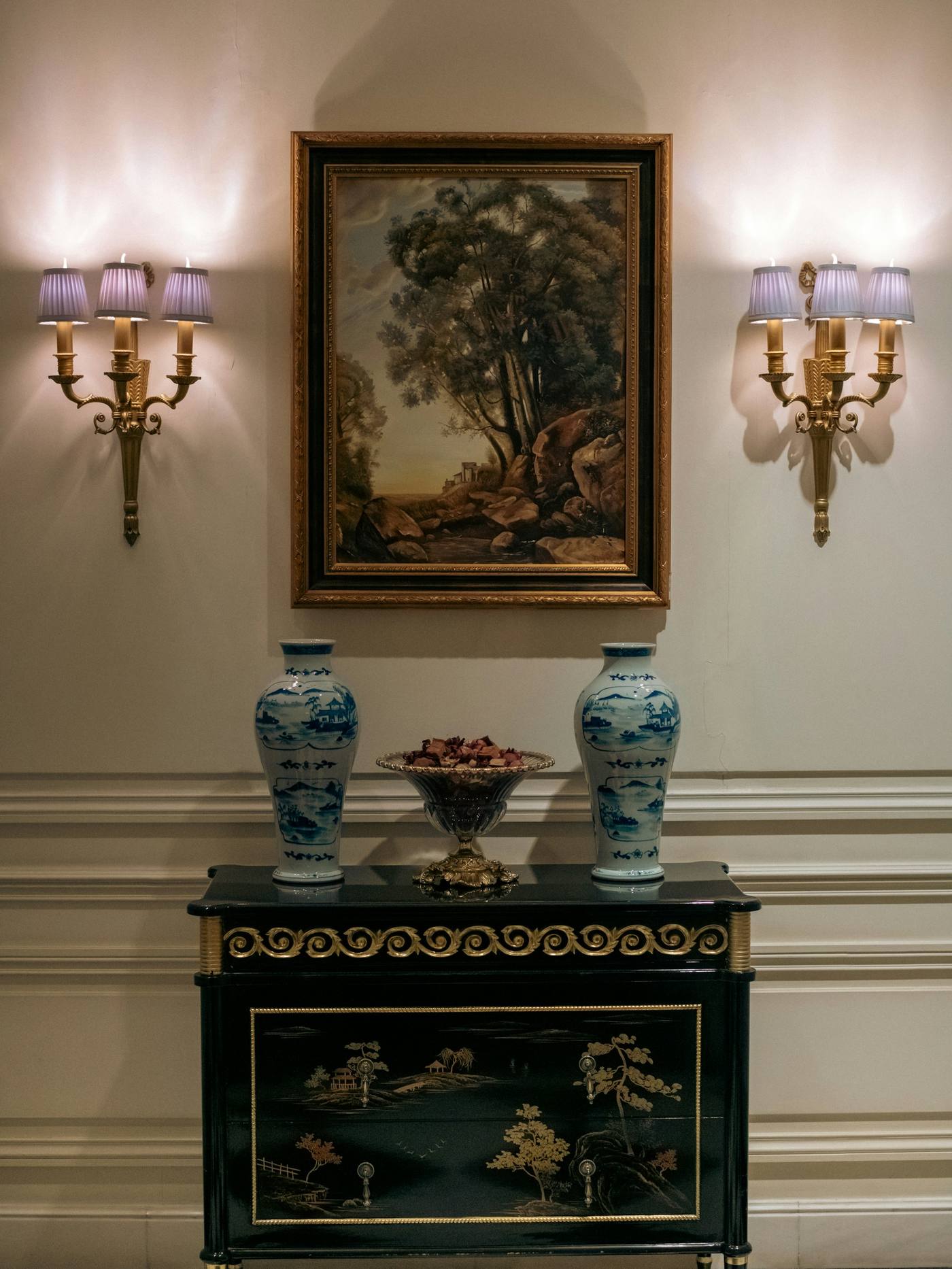 Aparador oscuro con jarrones azules y blancos, entre dos apliques de pared
