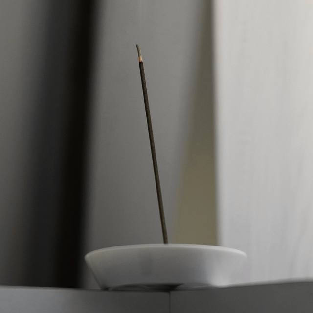 Una varilla de incienso en un soporte blanco junto a una pared clara