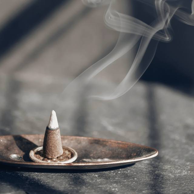 Un cono de incienso sobre un plato de metal bajo una luz con sombras