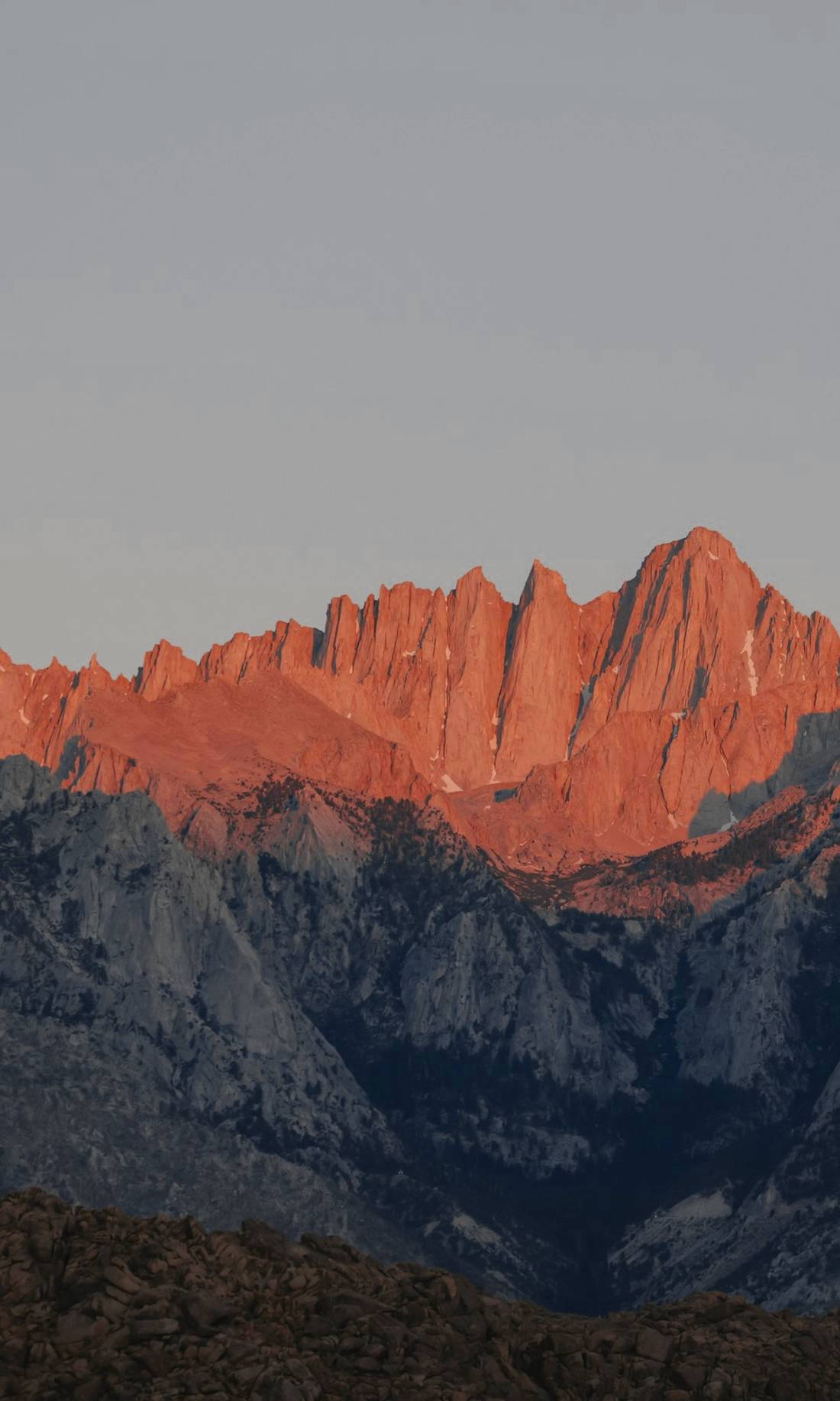 Picos de roca roja al atardecer con montañas grises al fondo