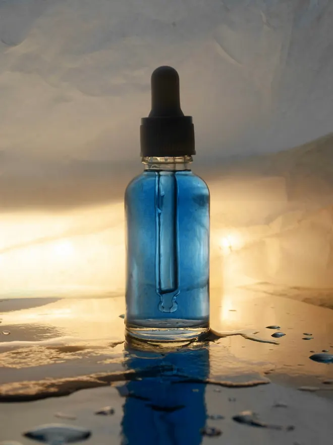 Un frasco de vidrio azul con gotero a contraluz, con luz dorada de atardecer