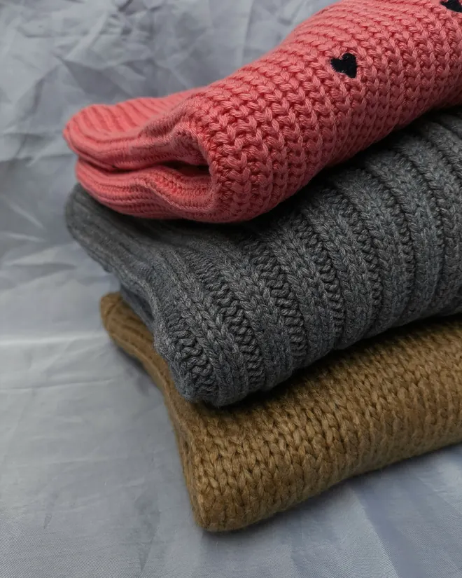 Tres prendas de punto dobladas: coral, gris y camel