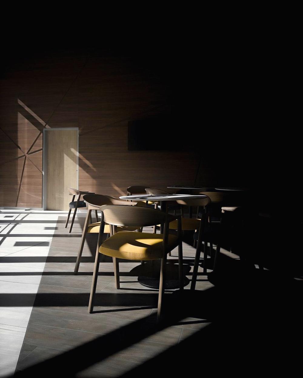 Sala en penumbra con sillas y una franja de luz en el suelo