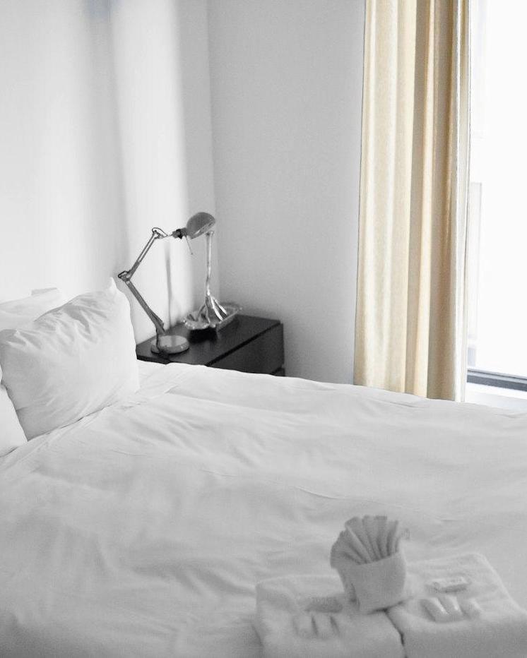 Cama blanca junto a una ventana con cortinas claras