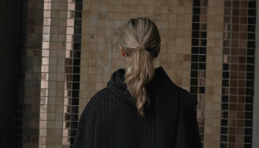 Una mujer de espaldas con un abrigo largo de lana oscura frente a un muro de mosaicos
