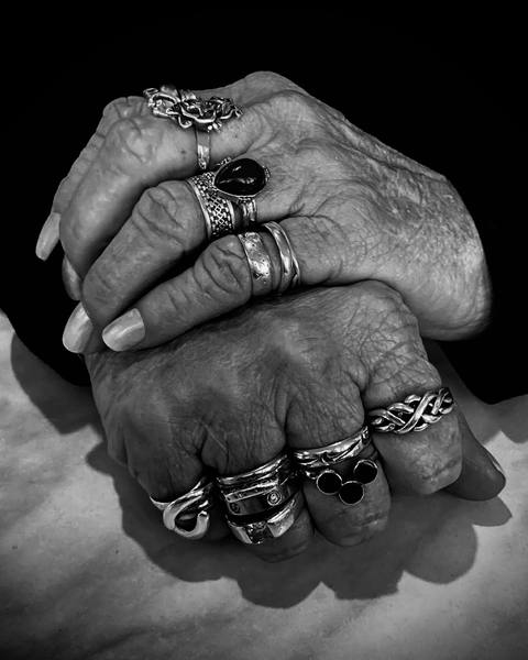 Manos entrelazadas con varios anillos de plata, en blanco y negro