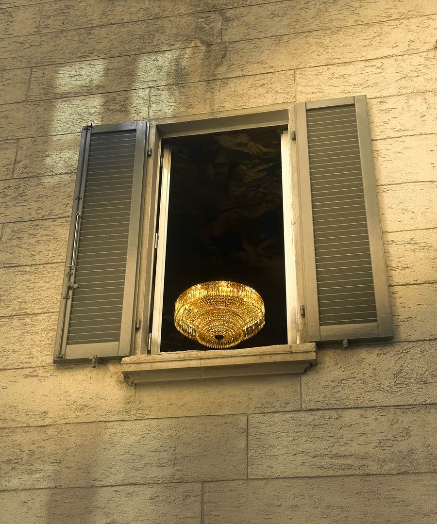Una ventana con postigos abiertos y una lámpara dorada encendida