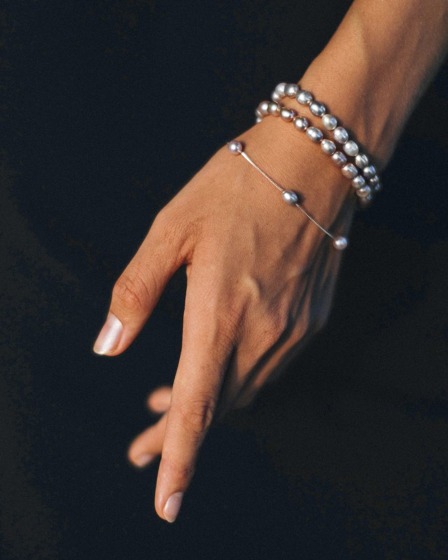 Una mano con dos pulseras de perlas sobre un fondo azul noche
