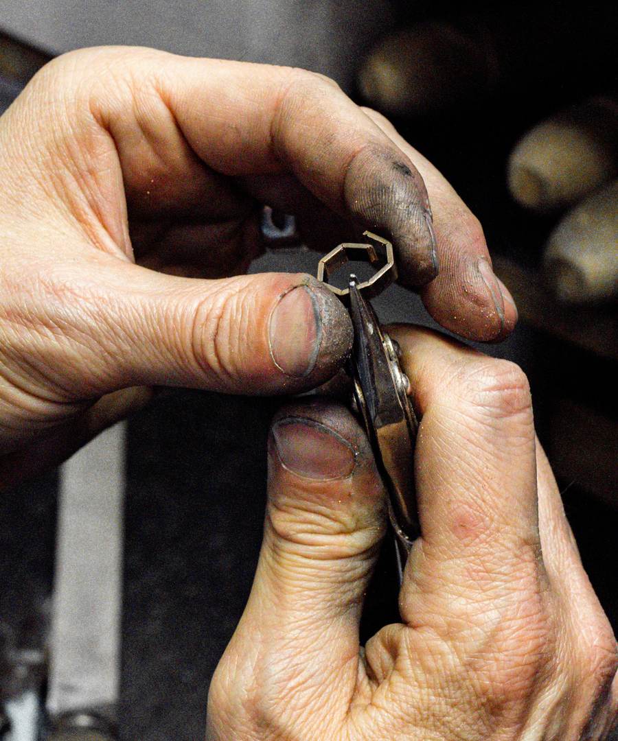 Manos de orfebre sujetando una pieza pequeña de metal