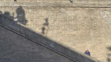 Muro de ladrillo con una escalera diagonal y una figura diminuta