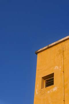 Esquina amarilla con una ventana pequeña contra un cielo azul