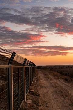 Camino de tierra junto a una valla y nubes rojizas