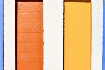 Dos columnas, una naranja y otra amarilla, contra un muro blanco