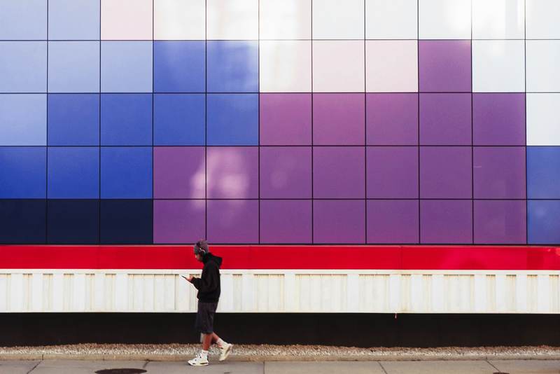 Fachada de paneles azules y violetas con una figura que camina delante