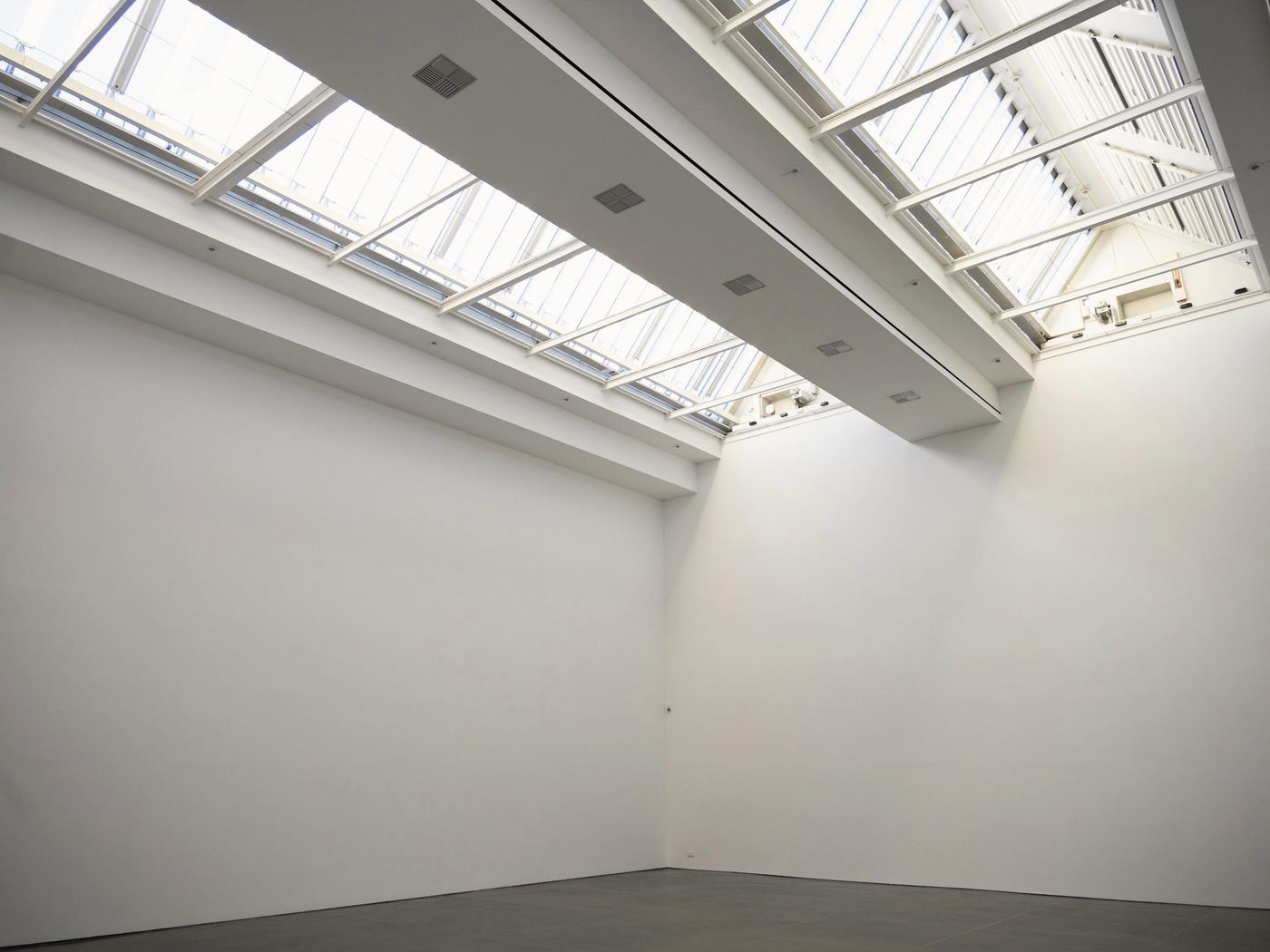 Sala amplia de muros blancos con obra sobre papel en la pared del fondo y un banco de madera
