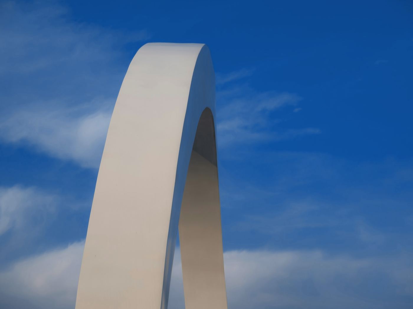 Un arco blanco de gran escala recortado contra un cielo azul con nubes