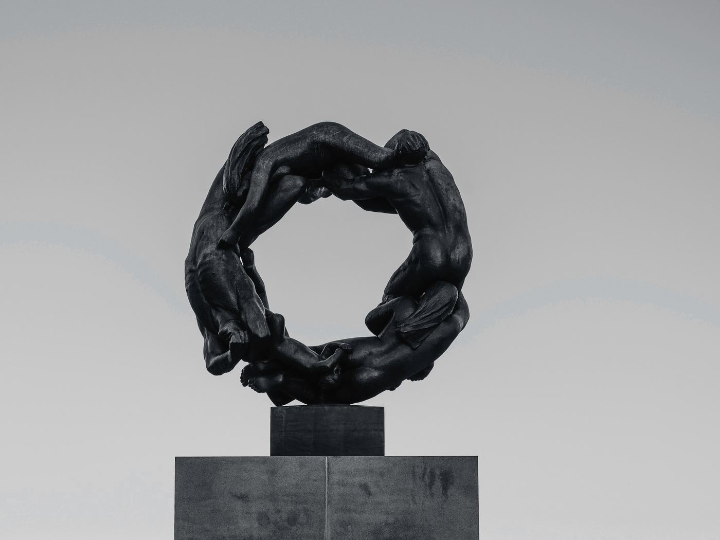 Anillo de bronce oscuro con figuras entrelazadas sobre un pedestal de piedra