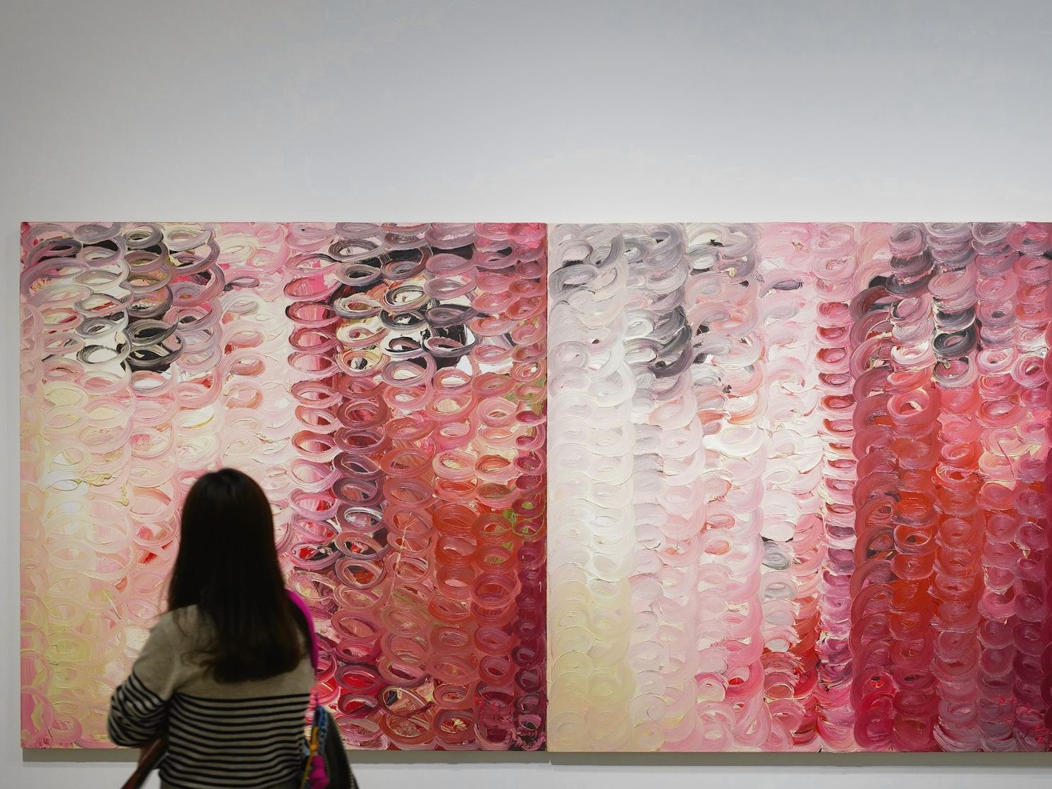 Una visitante de espaldas ante una pintura de gran formato en tonos rosados y rojos sobre un muro gris claro