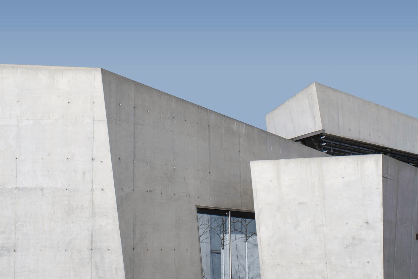 Edificio de hormigón con cubos superpuestos y una entrada vidriada bajo un cielo azul