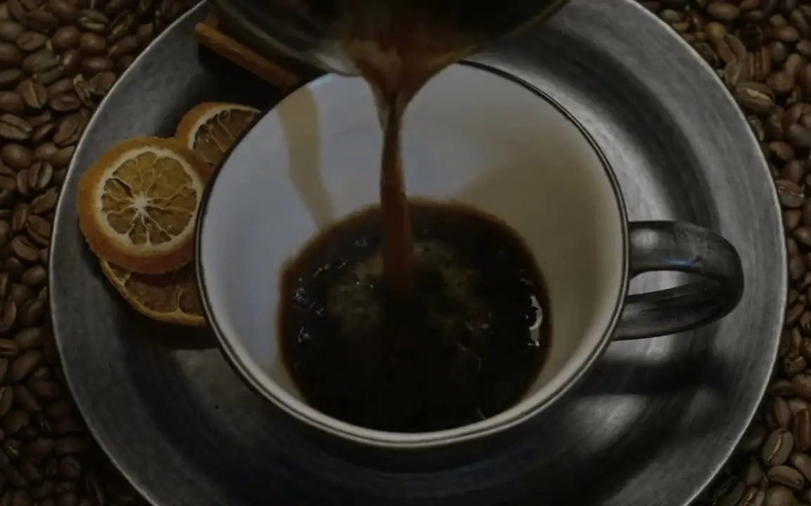 Café cayendo en una taza blanca rodeada de granos