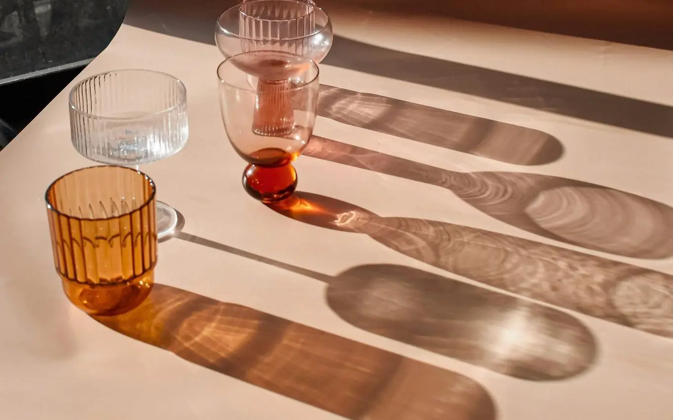 Copas de vidrio de colores y sus sombras largas sobre una mesa clara