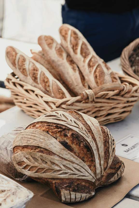 Una hogaza con cortes en forma de hoja junto a una canasta de baguettes