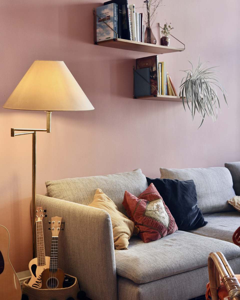 Rincón con muro rosa, sofá claro, lámpara de pie y estantes con libros
