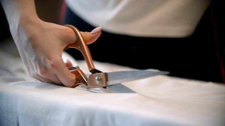 Unas tijeras de sastre cortan una tela blanca sobre la mesa