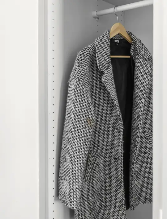 Abrigo de tweed gris colgado en un armario blanco