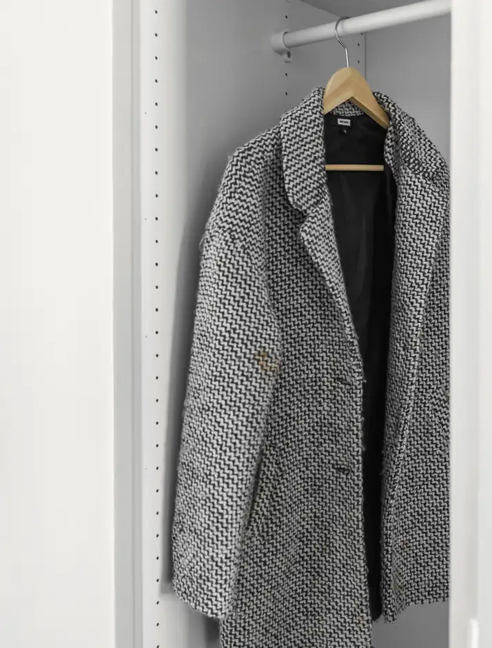 Abrigo de tweed gris colgado en un armario blanco