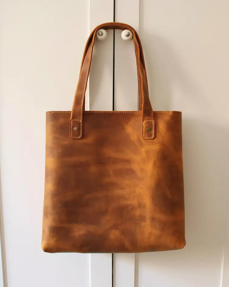 Bolso de cuero color miel colgado de una puerta blanca