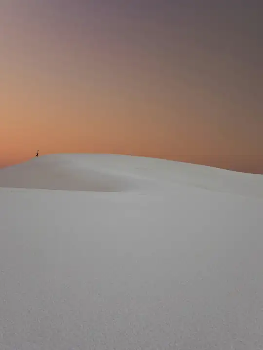 Duna de nieve y una figura minúscula bajo un cielo anaranjado
